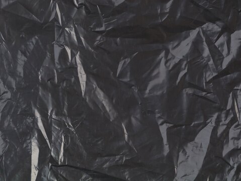 Close up view of dark crumpled black plastic sheet texture. Abstract wrinkled polyethylene bag surface background for modern design, grunge wallpaper, and packaging pattern concept