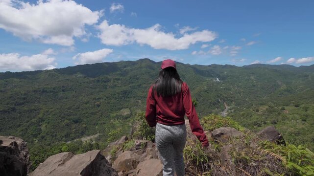 Asian Young Woman Jumps On Rocks on A Mountain and Looks Around in Asia, Travels through the Jungle among Palm Trees in Sunny Weather