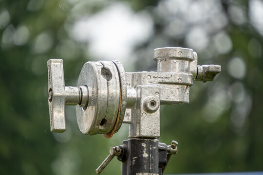 A heavy-duty silver metal grip head with a T-handle tightening knob is mounted on a light stand against a soft green foliage background.