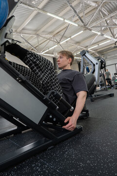 Young man performing heavy leg press in modern gym with industrial ceiling and strength equipment