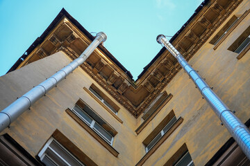 Two metal rain downspout gutters attached to a yellow stucco wall of a classic vintage residential apartment building architecture structure. Old municipal drainage utility system engineering, house.  © Dmitry Presnyakov
