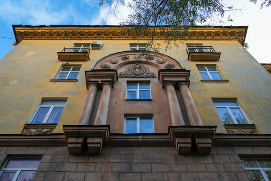 Beautiful bas relief and columns on a yellow stucco facade of a classic stalinist empire apartment building architecture structure. Old soviet residential house exterior with decorative molding. 