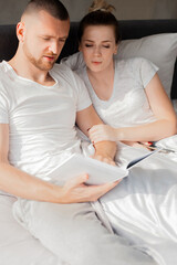 Couple reading book together while sitting in bed by window © Mirrorstudio