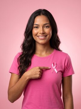 outubro rosa &mdash; mulher brasileira sorrindo aponta para a fita rosa na camiseta, conscientiza&ccedil;&atilde;o sobre o c&acirc;ncer de mama em fundo rosa.