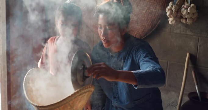Steam rises from a woven bamboo basket as sticky rice steams over a clay pot, with a daughter sitting nearby in a rural Thai kitchen.