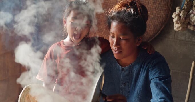 Steam rises from a woven bamboo basket as sticky rice steams over a clay pot, with a daughter sitting nearby in a rural Thai kitchen.