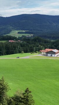 Top view of traditional country houses surrounded by green fields, forests and hills in the foothills of the Alps. Concept of country vacation, farming, sustainable development and European nature