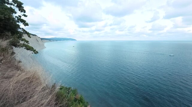 Scenic coastal view featuring a small boat navigating the calm blue waters under a clear sky with scattered clouds and a grassy shoreline in the foreground