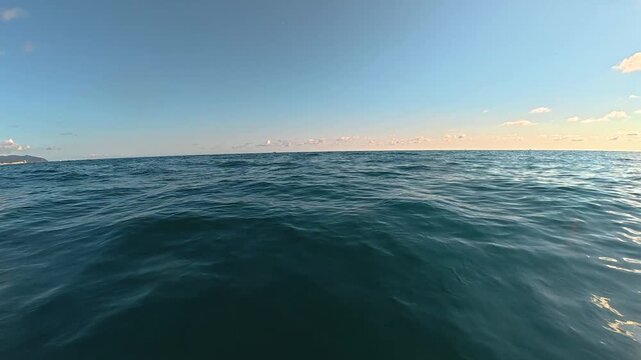 Expansive view of tranquil ocean waters under a clear blue sky with scattered clouds and distant coastal landscape visible along the horizon