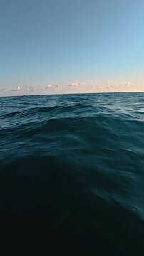 Expansive view of tranquil ocean waters under a clear blue sky with scattered clouds and distant coastal landscape visible along the horizon