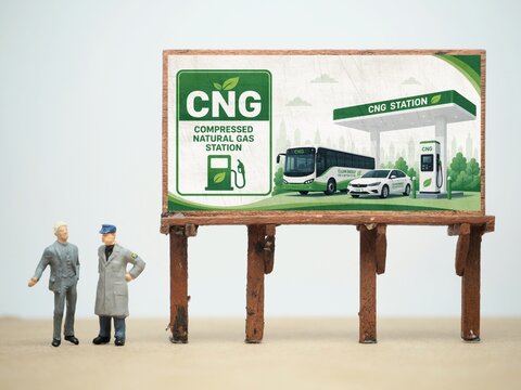Mini toy of action figure at studio with blurred background. Miniature photography concept design. Minifigure of people with Compressed Natural Gas CNG Station illustration picture at billboard.