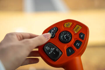 A hand operates an orange push-button joystick controller for agricultural machinery against a softly blurred background. © Marina