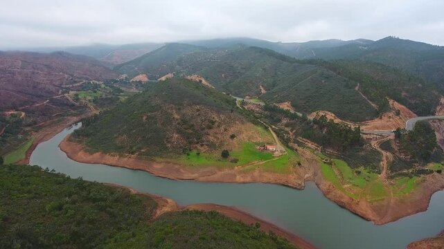 Dramatic aerial view capturing the contrast between lush green hills and the devastating effects of forest fires on the landscape surrounding a winding river in monchique, portugal