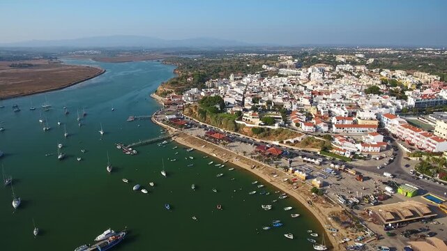 Beautiful aerial perspective of the charming fishing village of alvor, portugal, showcasing its picturesque harbor with many boats, the river estuary, and the traditional whitewashed houses