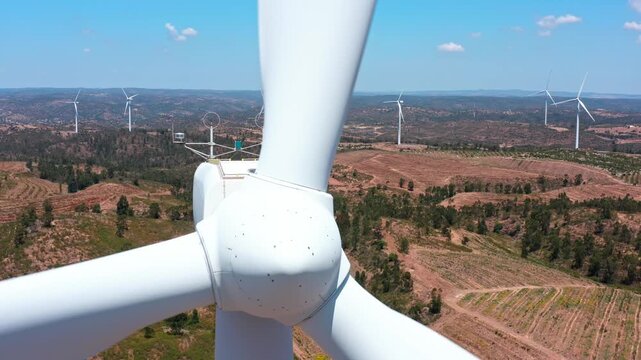 Extreme close up aerial shot of a large wind turbine's rotor and blades spinning to generate clean, renewable energy over a rural landscape on a sunny day with blue sky in the background
