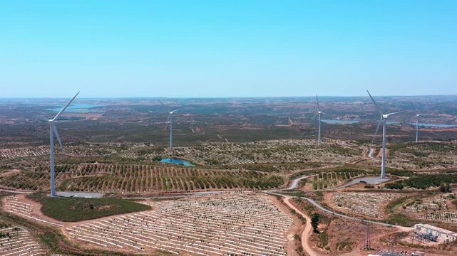 Aerial view of a wind farm with rotating turbines and a solar panel field generating clean, renewable energy under a clear blue sky, promoting sustainability and fighting climate change