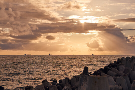 Golden sunset over ocean waves along concrete breakwater rocks