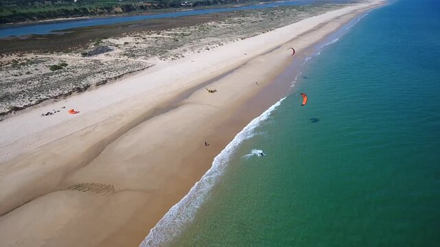 Beautiful aerial drone perspective of a wide sandy coastline with athletes kitesurfing and enjoying extreme water sports in the turquoise sea on a sunny day during the summer holidays