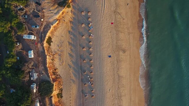 Majestic aerial view of a golden sandy beach in algarve, portugal, with gentle waves from atlantic ocean washing ashore as warm light of sunset casts long shadows from the parasols. Loule Velho