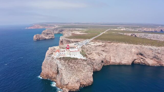 Drone circling farol do cabo de sao vicente on dramatic cliffs at sagres, algarve, overlooking the atlantic ocean  iconic seascape, coastline, and coastal landmark
