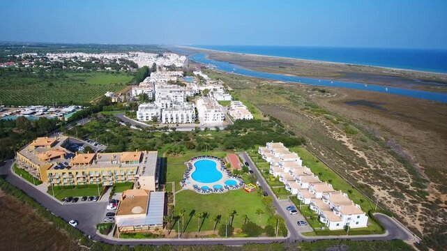 Beautiful aerial descending view of a luxury hotel resort with a swimming pool and apartment buildings located on the sunny coast of cabanas de tavira in algarve, portugal near the ocean