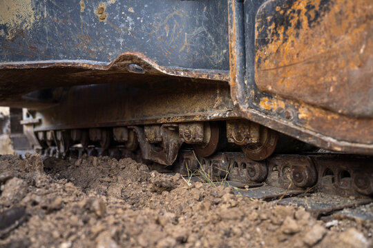 Close-up of muddy metal tracks and rollers on heavy construction machinery resting on loose soil.