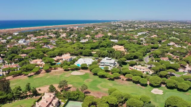 Aerial view of an exclusive residential area with luxury villas, swimming pools, and a lush green golf course along the beautiful coastline of vale do lobo in algarve, portugal