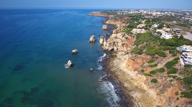 Drone flying over the beautiful algarve coastline with stunning rock formations, turquoise ocean water, and the town of albufeira with its white houses on a sunny day in southern portugal