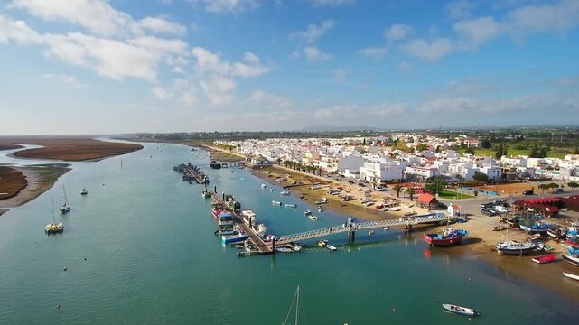 Picturesque aerial establishing shot of the charming fishing village of santa luzia, showing its whitewashed houses, harbor with boats, and the beautiful ria formosa natural park coastline