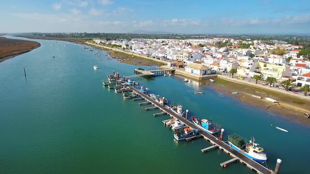 Aerial footage moving over traditional fishing boats moored at the dock in the charming village of santa luzia, with the scenic ria formosa estuary and whitewashed houses in the algarve region
