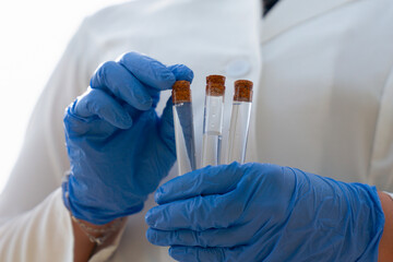 Obraz na płótnie Canvas pneumonic plague outbreak scientist holding test tube sample, focused female epidemiologist in lab coat, face mask and blue gloves examining sample looking away from camera, forest and sky with copy s