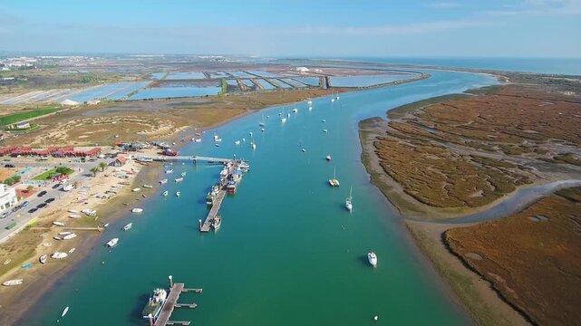 Panoramic aerial view flying over the picturesque fishing village of santa luzia, showing the harbor with boats moored at the pier and the scenic landscape of the ria formosa natural park