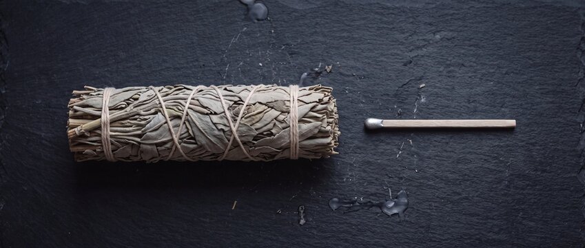Natural white sage smudge stick and match on dark slate background, used for cleansing and purification rituals