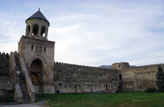 The stone belfry gatehouse and crenelated defensive walls enclose a grassy courtyard at the Svetitskhoveli Cathedral complex in Mtskheta, Georgia