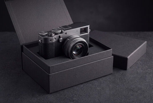 Compact digital camera inside open matte black packaging box on dark background