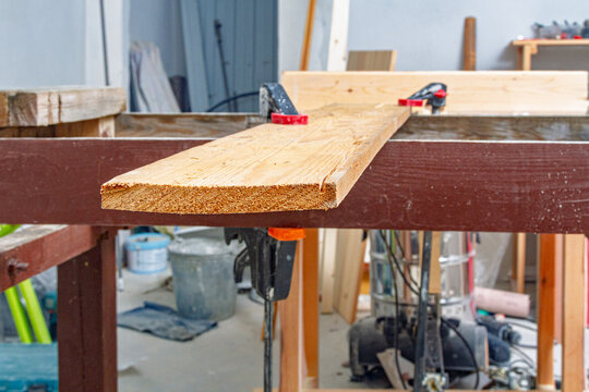 Wood plank secured with clamps on a workbench in a woodworking shop. Carpentry and lumber preparation for furniture making. DIY woodworking project. Workshop craft and home improvement