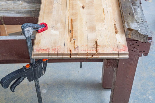 Wooden parquet boards held by a clamp on a workbench during woodworking. Lumber preparation for carpentry and DIY construction. Workshop craft and repair. Home improvement project