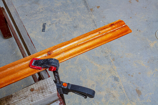 Wooden plank secured with a clamp on a sawhorse in a workshop. Carpentry and woodworking project. Lumber preparation for repair and construction. DIY home improvement