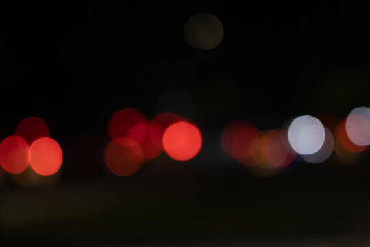 Abstract out of focus night bokeh lights with warm red and cool white circular orbs on dark background.
