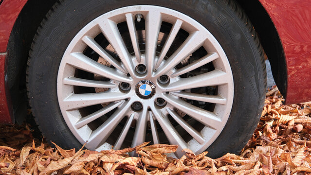Nahaufnahme einer Leichtmetallfelge an einem roten BMW-Fahrzeug, das im herbstlichen Laub geparkt ist. Z&uuml;rich 3.10.2026