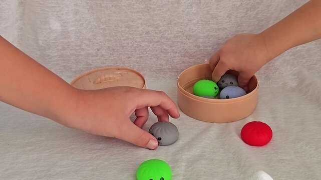 Children hands packing and putting colorful dumpling squishy toys inside food steamer container and closing lid, 4K slow motion close up video