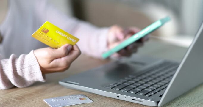 Close-up of a woman holding a credit card while using a laptop for online payment. e-commerce, secure digital transaction, online shopping, fintech, and cashless payment