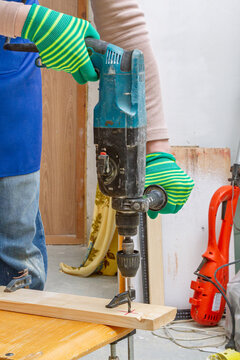 A worker drills a wooden board with a hammer drill in a workshop. Woodworking and home improvement. Construction, renovation, and craft projects. Using power tools and skilled work