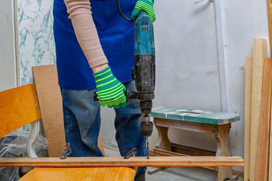 Person drills a wooden board with a hammer drill in a workshop. DIY carpentry and woodworking. Furniture repair and restoration. Practical construction and DIY craft work
