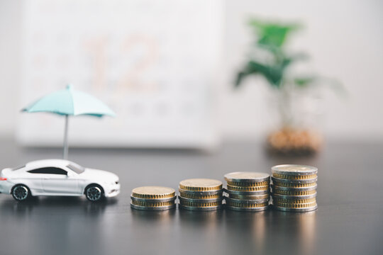 White toy car under a blue umbrella beside rising coin stacks, symbolizing auto insurance cost, premium growth, vehicle protection, savings, risk management and financial planning.