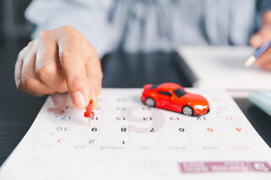 Person marking a calendar date beside a model car, representing car payment scheduling, purchase planning, loan due dates, budgeting, monthly expenses, deadlines and vehicle finance.