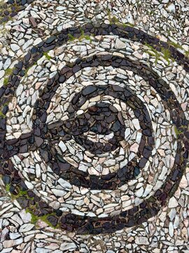 Top view texture of a circular spiral stone mosaic pattern on the floor.