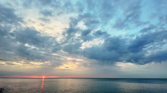 Dramatic clouds over a calm sea with a red sunset glow on the horizon.