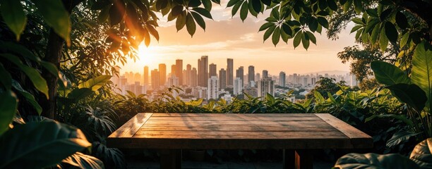 Fototapeta premium Wooden table on terrace with green leaves. Beautiful sunset illuminates urban city skyline in background. Peaceful outdoor scene with warm sunlight, tropical foliage. Relaxing view of cityscape from