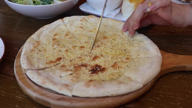 Close up hands using knife cutting and taking slice of hot cheese pizza flatbread from wooden board. Italian cuisine, baked focaccia dining appetizer eating in restaurant meal concept